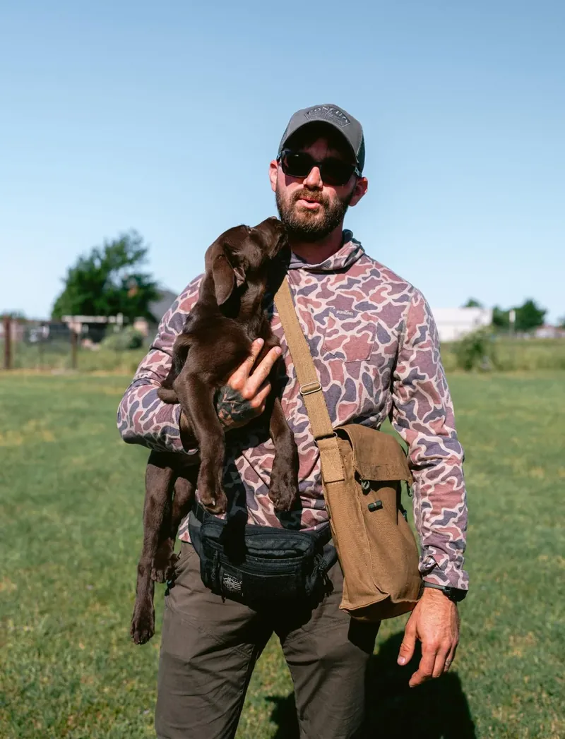 Justin Rie, Master Trainer for Off Leash K9 Training Boca Raton, holding a chocolate Labrador puppy in a training field